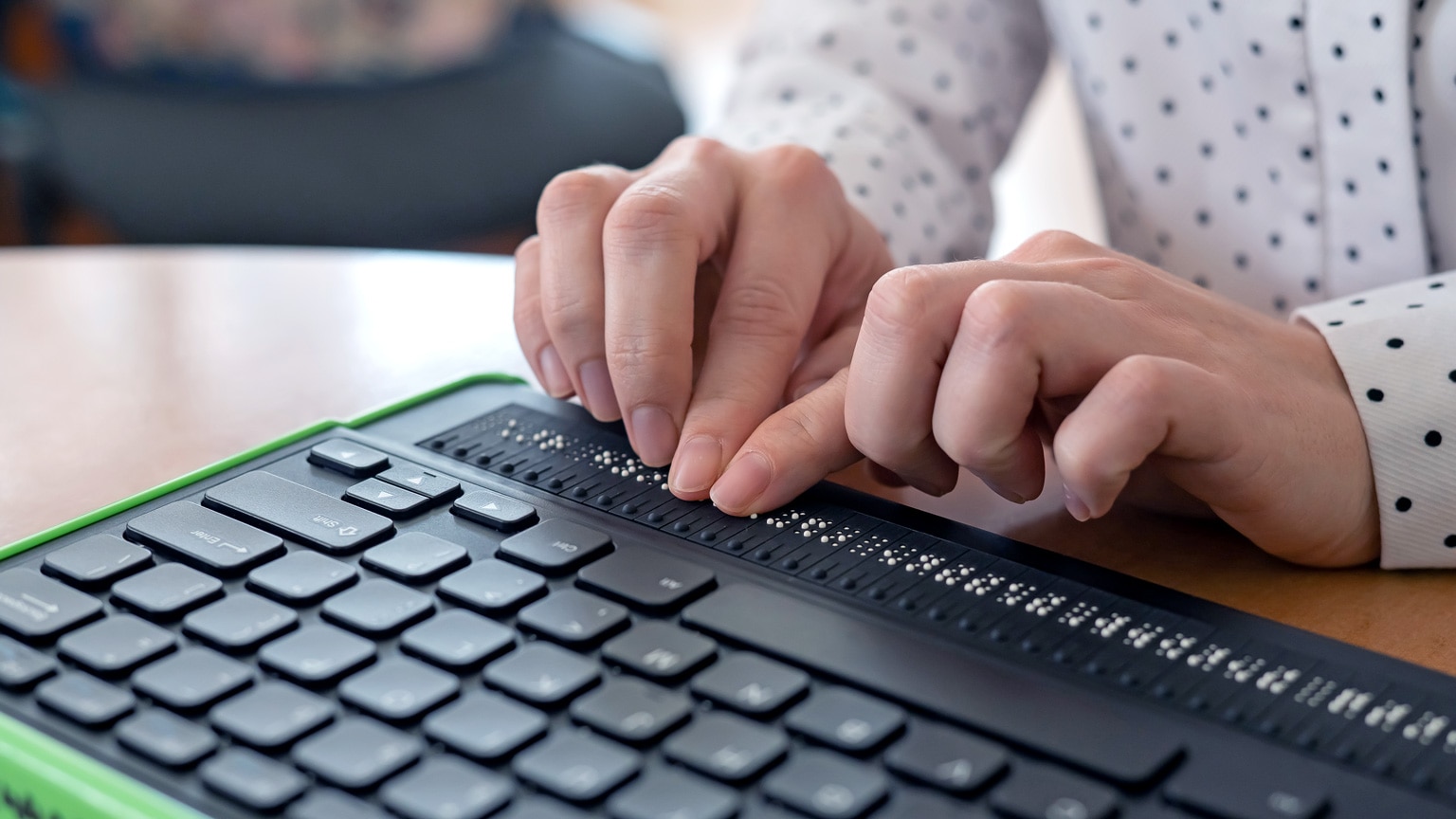 Close up photograph of a woman's hands using a Braille keyboard.